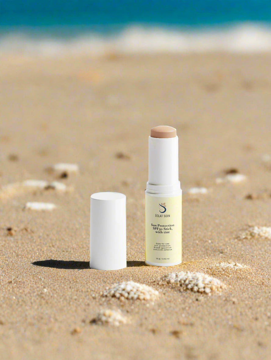 Eclat Soin SPF50 Sun Protection Stick with Tint on sandy beach, ideal for sun protection and easy application.